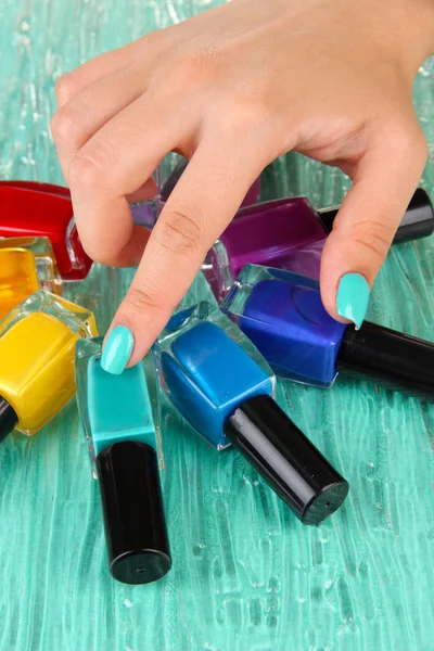 Hermosas manos de mujer con manicura azul y varias botellas con esmalte de uñas, sobre fondo de color — Foto de Stock