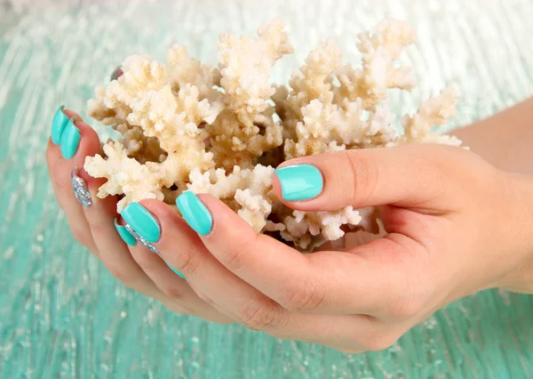 Hermosas manos de mujer con manicura azul sosteniendo coral, sobre fondo de color —  Fotos de Stock