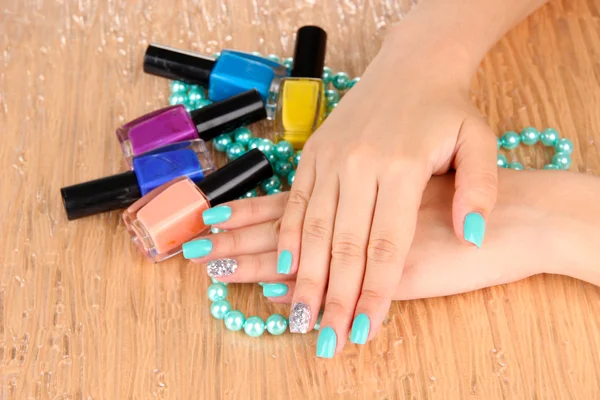 Beautiful woman hands with blue manicure holding beads and bottles with nail polish, on color background — Stock Photo, Image