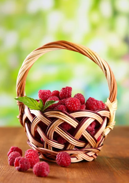 Framboesas doces maduras na cesta na mesa de madeira, no fundo verde — Fotografia de Stock