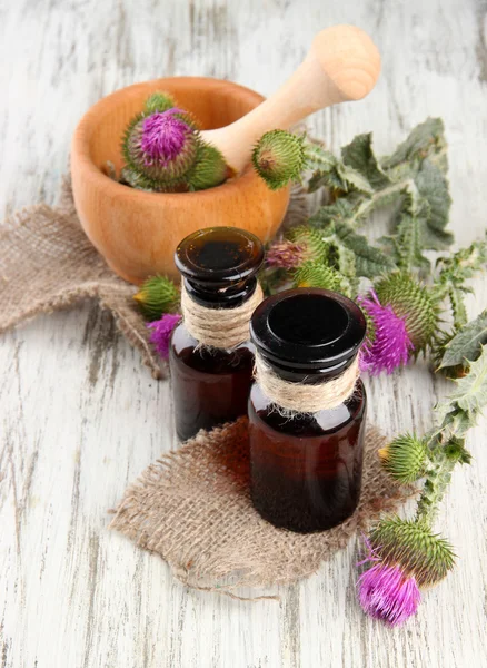 Medicine bottles and mortar with thistle flowers on wooden background — Stock Photo, Image