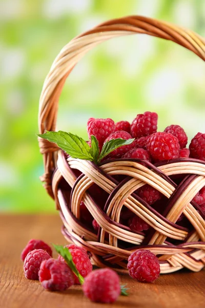 Framboesas doces maduras na cesta na mesa de madeira, no fundo verde — Fotografia de Stock