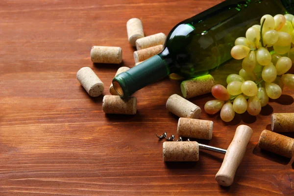 Bottle of wine, grapes and corks on wooden background — Stock Photo, Image