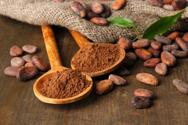 Cacao en polvo en cucharas y granos de cacao sobre fondo de madera — Foto de Stock