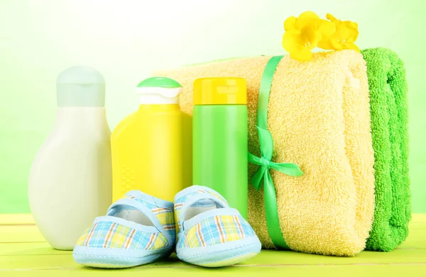 Cosméticos para bebês, toalhas e botas na mesa de madeira, no fundo verde — Fotografia de Stock