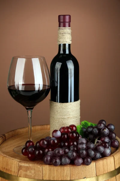 Composition of wine bottle, glass of red wine, grape on wooden barrel, on color background — Stock Photo, Image