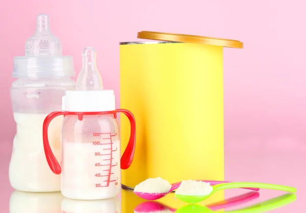 Garrafas com leite e alimentos para bebês em fundo rosa — Fotografia de Stock