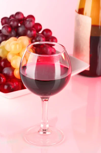 Glass of wine with lipstick imprint, grapes and bottle on pink background — Stock Photo, Image