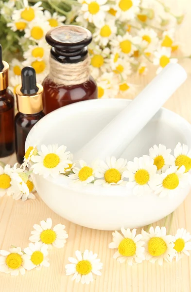 Aceite esencial y flores de manzanilla en mortero sobre mesa de madera —  Fotos de Stock