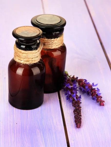 Medicine bottles and salvia flowers on purple wooden background — Stock Photo, Image