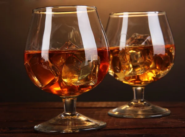 Copas de brandy con hielo sobre mesa de madera sobre fondo marrón —  Fotos de Stock
