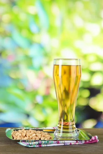 Beer in glass and nuts on table on nature background — Stock Photo, Image