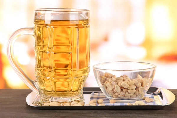 Cerveza en vidrio y nueces en bandeja sobre mesa de madera sobre fondo de habitación — Foto de Stock