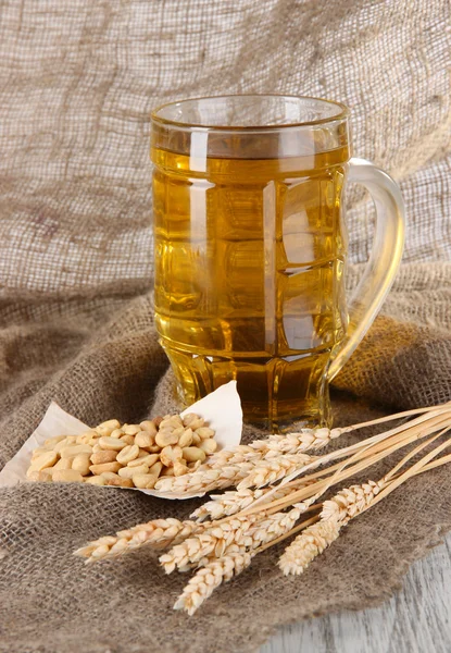 Cerveza en vaso y nueces en el ensacado sobre mesa de madera — Foto de Stock