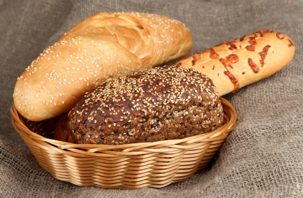 Baked bread in wicker basket on burlap background — Stockfoto