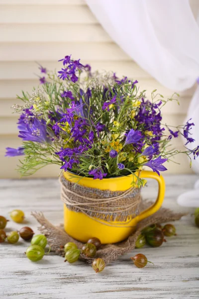 Hermoso ramo de flores silvestres en taza y bayas en mesa de madera — Foto de Stock