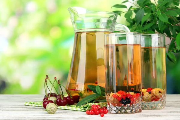 Кувшин и стаканы компота с летними ягодами на естественном фоне — стоковое фото