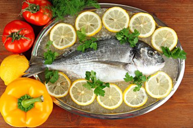 dorado fresco en tajadera con limón y verduras en la mesa de madera