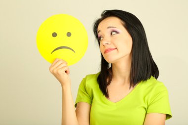 gri arka plan üzerinde üzgün smiley ile kağıt tutan genç kadın