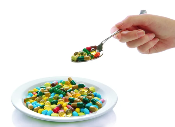 Colorful capsules and pills on plate with spoon in hand, close up — Stock Photo, Image