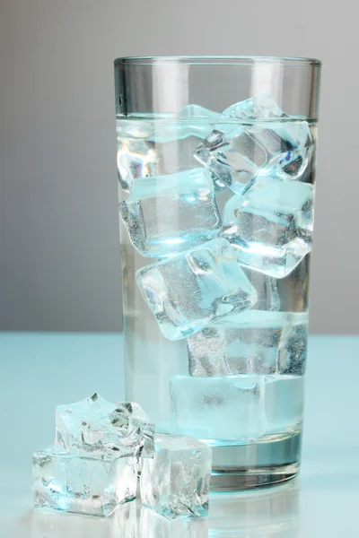Cubos de hielo en vidrio sobre fondo azul claro — Foto de Stock