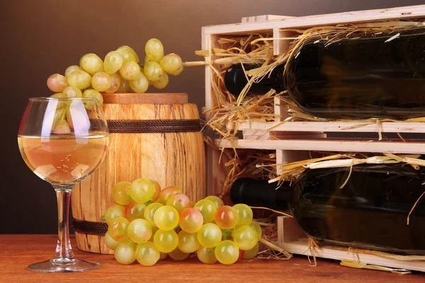 Boîtier en bois avec bouteille de vin, tonneau, verre à vin et raisin sur table en bois sur fond marron — Photo