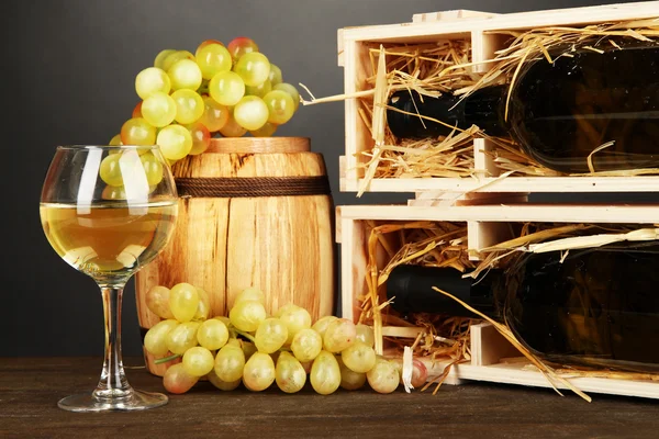 Деревянный чехол с винной бутылкой, бочкой, бочкой вина и виноградом на деревянном столе на сером фоне — стоковое фото
