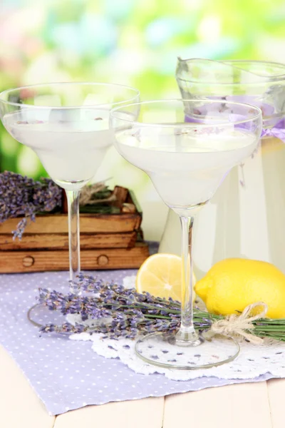 Lavender lemonade in glass jug and cocktail glasses, on bright background — Stock Photo, Image