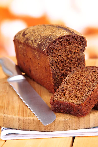 Sliced black bread and knife on chopping board on wooden table close up — Stock Photo, Image