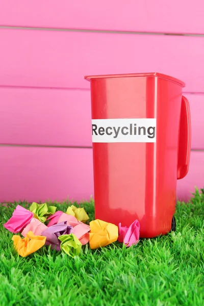 Cestino di riciclaggio con carte su erba su sfondo rosa — Foto Stock