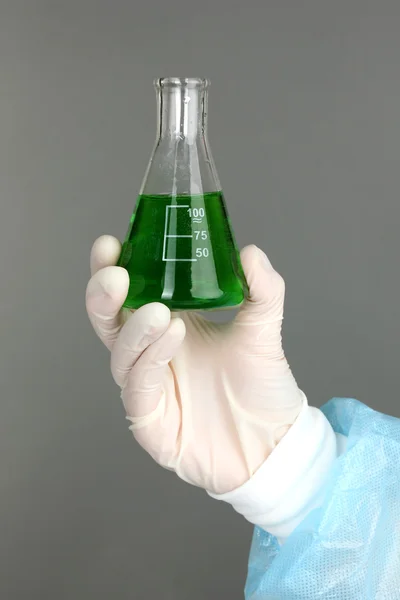 Glass tube with fluid in scientist hand during medical test on grey background — Stock Photo, Image