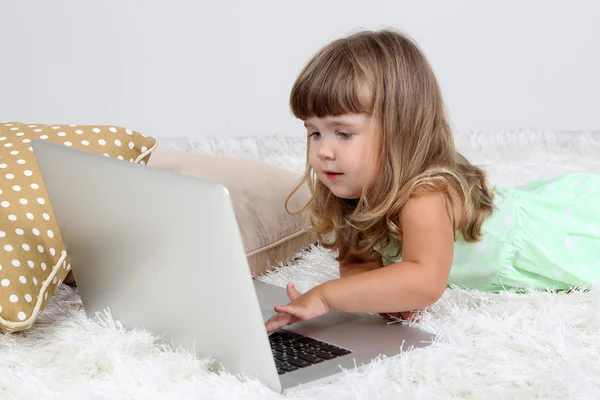 Lilla söta tjejen ligger på mattan med laptop, på grå bakgrund — Stockfoto
