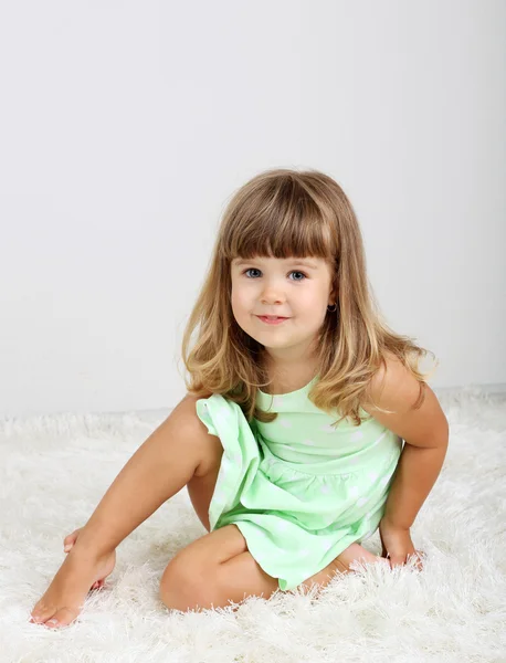 Little cute girl sitting on carpet, on gray background — Stock Photo, Image