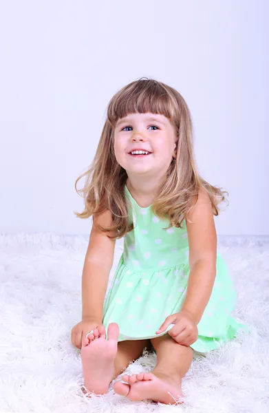 Little cute girl sitting on carpet, on gray background — Stock Photo, Image