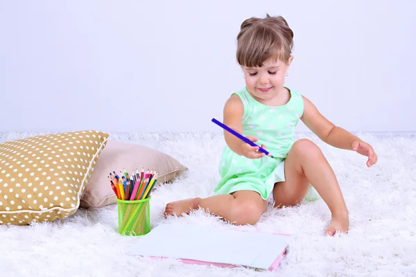 Niña linda sentada en la alfombra y dibujos, sobre fondo gris — Foto de Stock