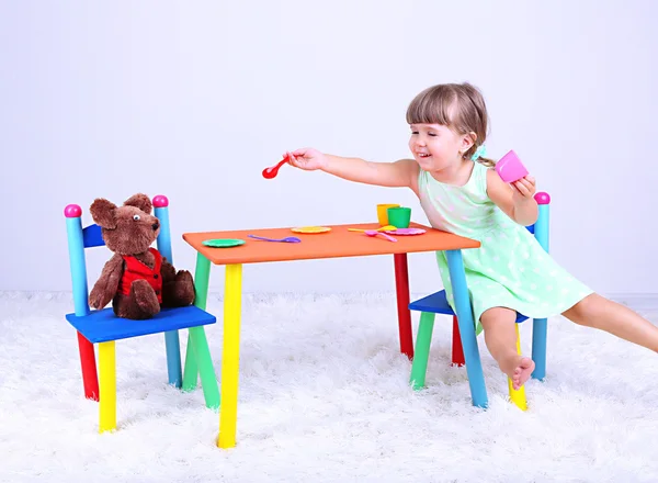 Pequena menina bonita sentada na pequena cadeira perto da mesa, no fundo cinza — Fotografia de Stock