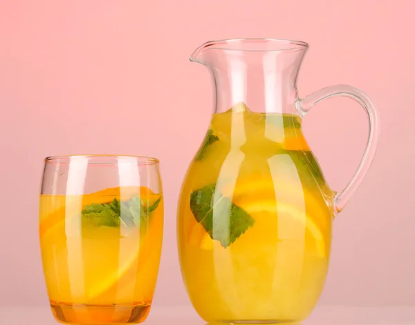 Citronnade orange en pichet et verre sur fond rose — Photo