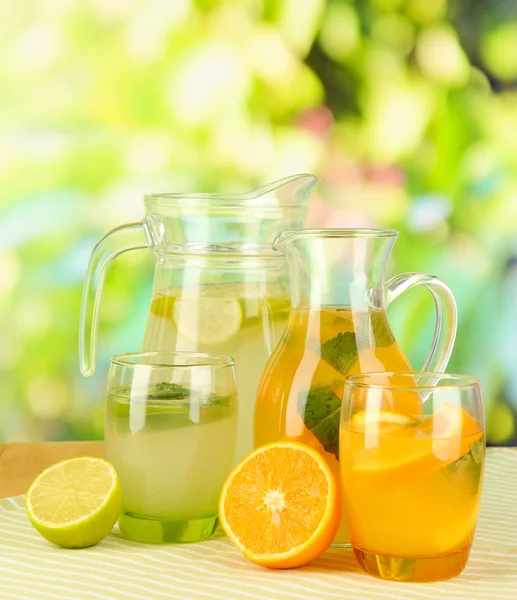 Limonada de naranja y limón en jarras y vasos sobre mesa de madera sobre fondo natural —  Fotos de Stock