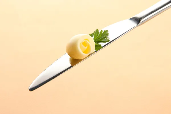 Butter curl on knife on beige background — Stock Photo, Image