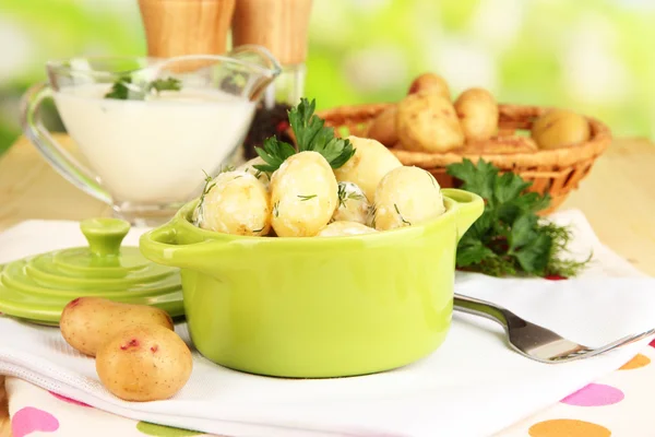 Batatas jovens macias com creme azedo e ervas na panela na mesa de madeira no fundo natural — Fotografia de Stock