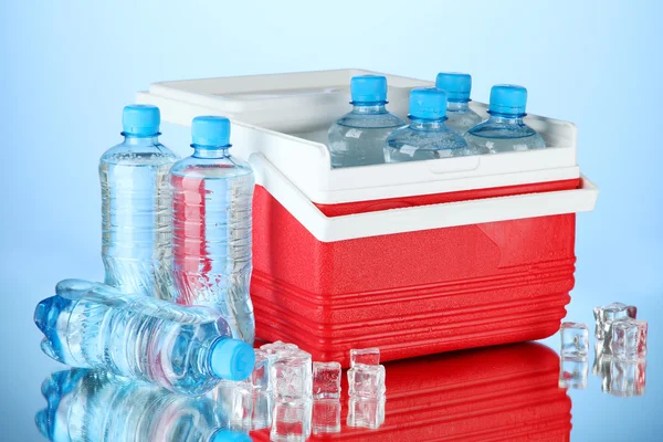 Refrigerador viajero con botellas de agua y cubitos de hielo, sobre fondo azul —  Fotos de Stock