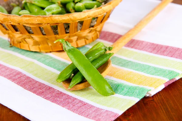 Green peas in wooden basket on napkin on table — Stock Photo, Image