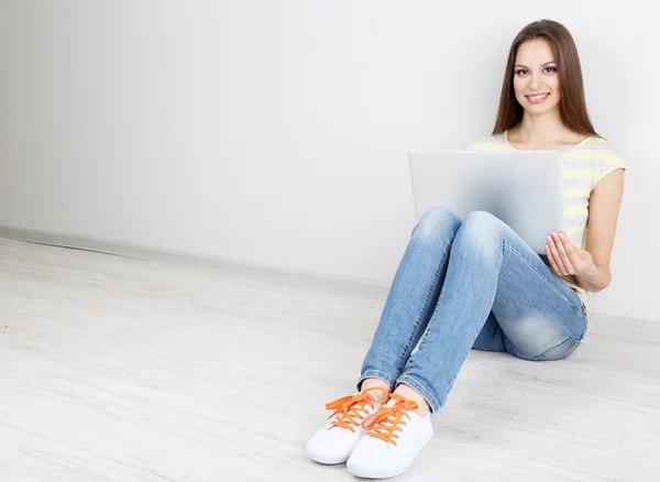 Hermosa joven sentada con portátil en la habitación — Foto de Stock