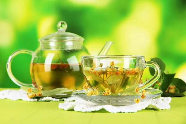 Hervidor de agua y taza de té con tilo sobre mesa de madera sobre fondo natural —  Fotos de Stock