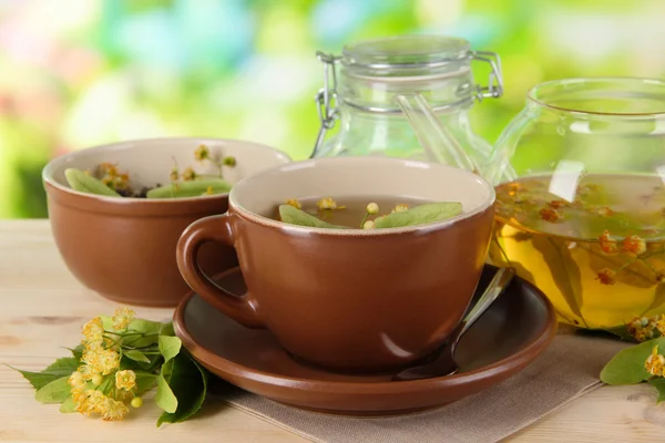 Hervidor de agua y taza de té con tilo sobre mesa de madera sobre fondo natural —  Fotos de Stock