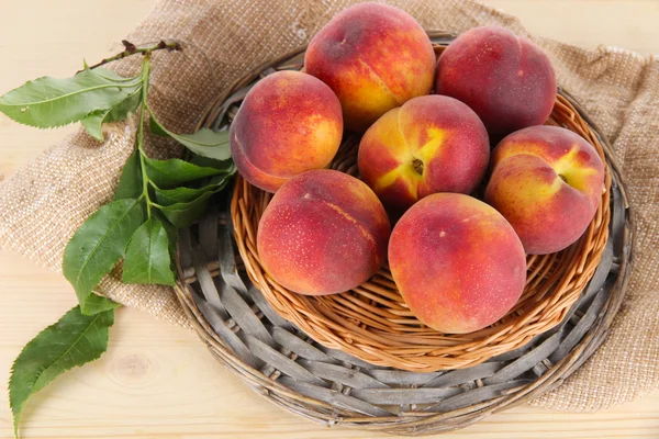 Peaches on wicker tray on sackcloth on wooden table — Stock Photo, Image
