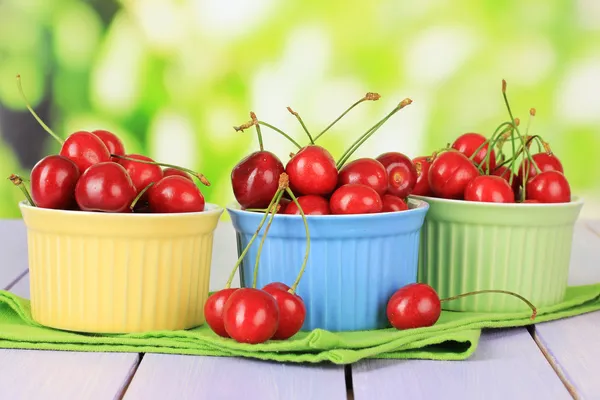 Cherry berries in bowls on wooden table on bright background — Stock Photo, Image
