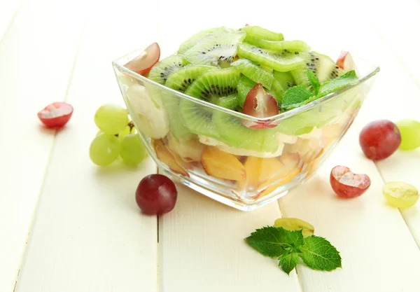 Salada de frutas saborosas em tigela de vidro, na mesa de madeira branca — Fotografia de Stock