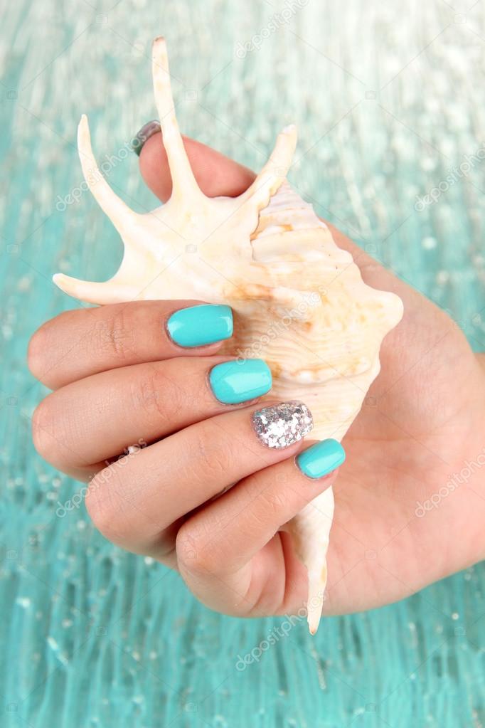 Beautiful woman hands with blue manicure holding shell, on color background