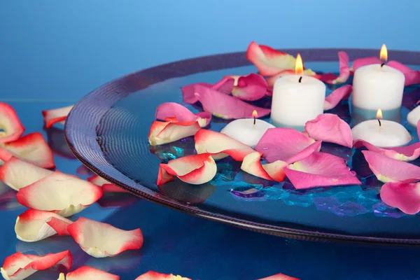 Rosenblätter und Kerzen in Wasser in der Vase auf blauem Hintergrund Nahaufnahme — Stockfoto